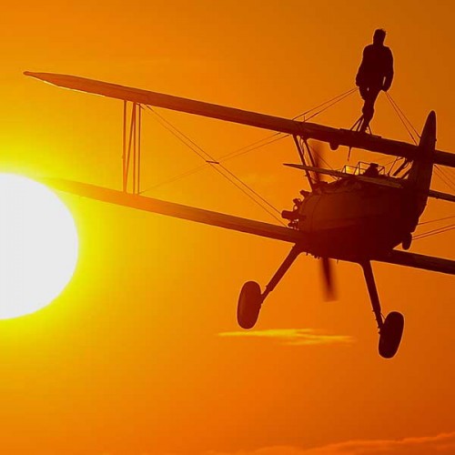 A plane and wing walker silhouetted by the sun set