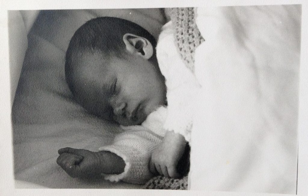 A black and white photo of a baby lying down, asleep 