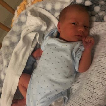 A newborn baby lying in a cot and looking at the camera