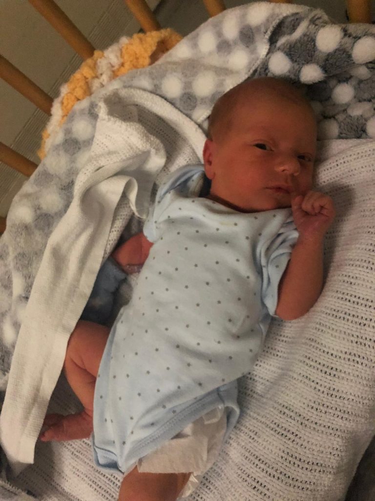 A newborn baby lying in a cot and looking at the camera