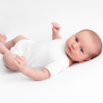 A white background with a baby looking at the camera, wearing a white babygrow