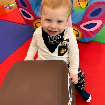 a toddler is smiling at the camera and sitting on a large toy