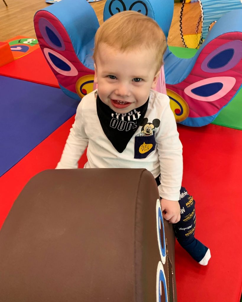 a toddler is smiling at the camera and sitting on a large toy