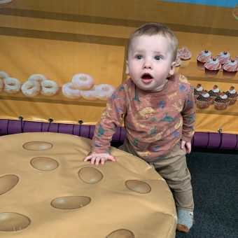 a toddler is standing up and leaning on a large toy looking surprised and staring slightly upwards