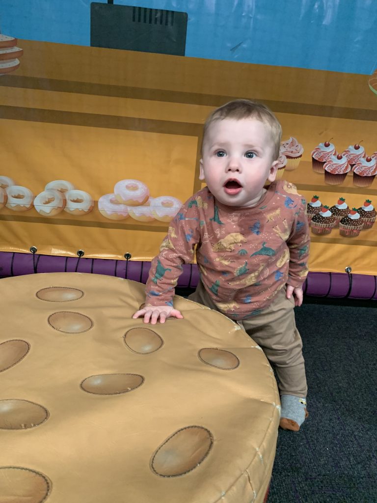 a toddler is standing up and leaning on a large toy looking surprised and staring slightly upwards