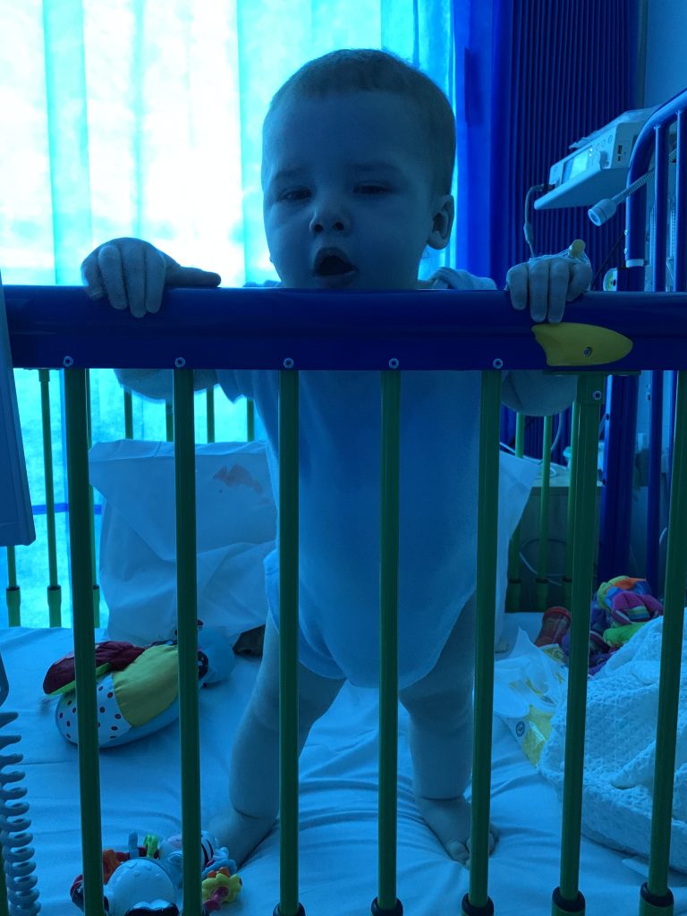 a baby is standing up and leaning on the edge of a cot