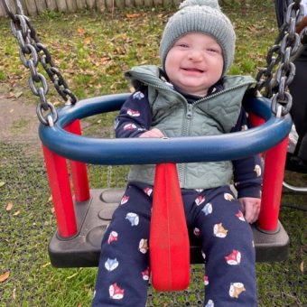 A baby in a swing smiling at the camera