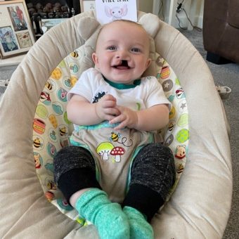 A baby in a baby seat with a sign saying 'goodbye wide smile'