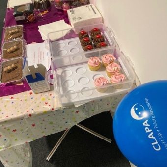 A bake sale table with cakes and a blue CLAPA balloon