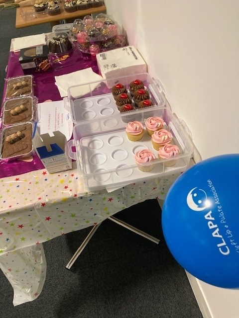 A bake sale table with cakes and a blue CLAPA balloon