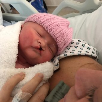 Newborn baby in a pink hat wrapped in a cream blanket
