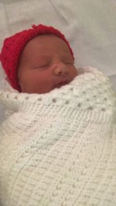 A baby in a red hat wrapped in a white blanket