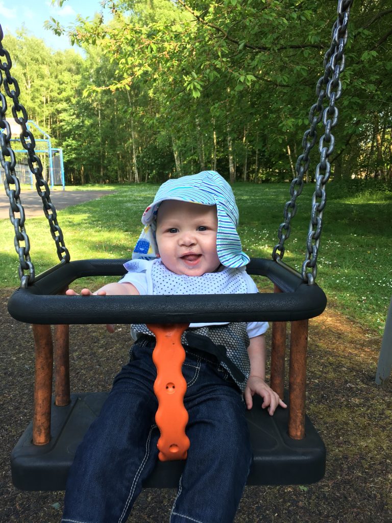 A baby sitting in a swing in a park wearing blue