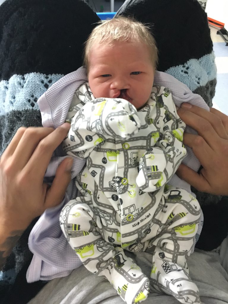 A new born baby wearing a white, grey and green babygrow