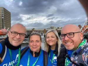 Two male and two female fundraisers wearing blue CLAPA t-shirts again a city skyline.