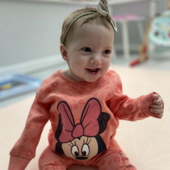 A baby girl smiling wear a orange minie mouse jumper