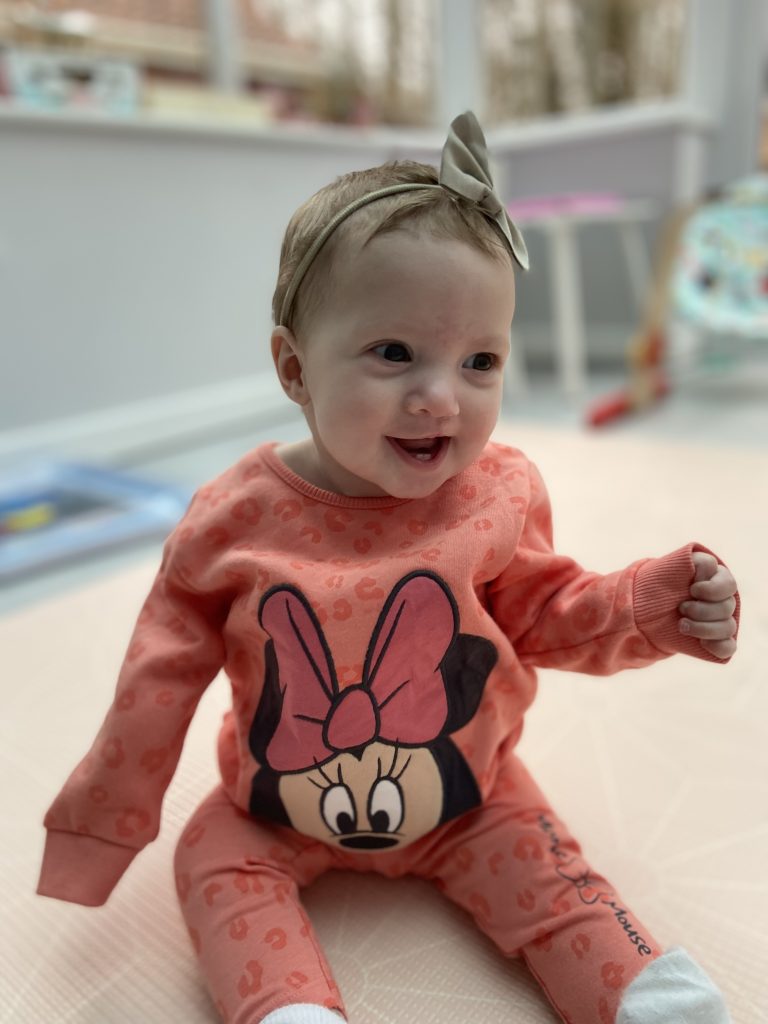 A baby girl smiling wear a orange minie mouse jumper