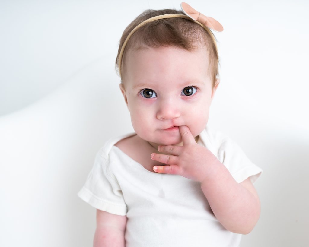 A baby girl wearing a white t-shirt and gold bow headband