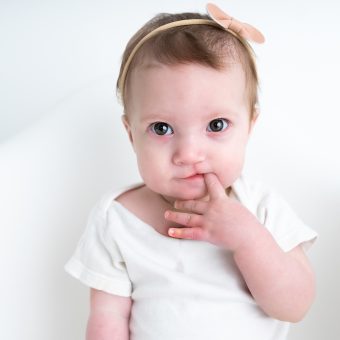 A baby girl wearing a white t-shirt and gold bow headband