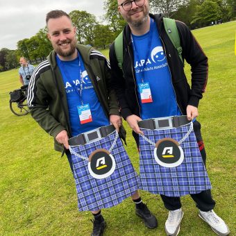 Two men in CLAPA Tshirts holding kilts