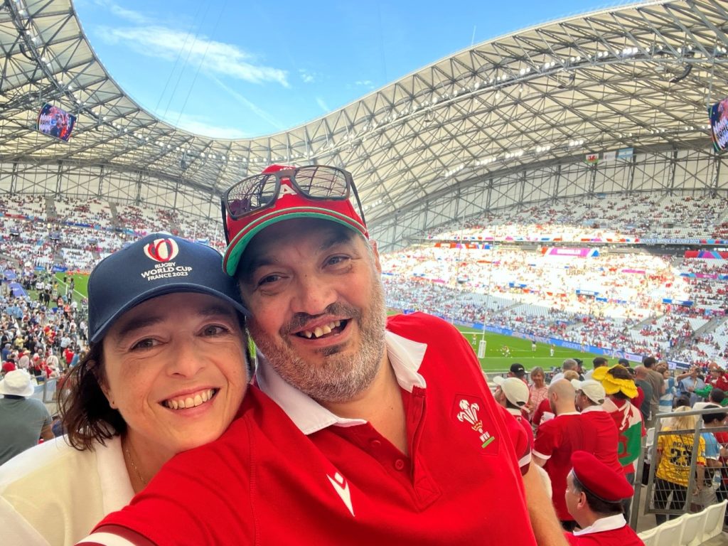 Photograph of Gareth, who was born with a cleft, and his wife at a rugby stadium during a match.