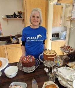 Karen wearing CLAPA branded t-shirt standing in front of bake sale cakes