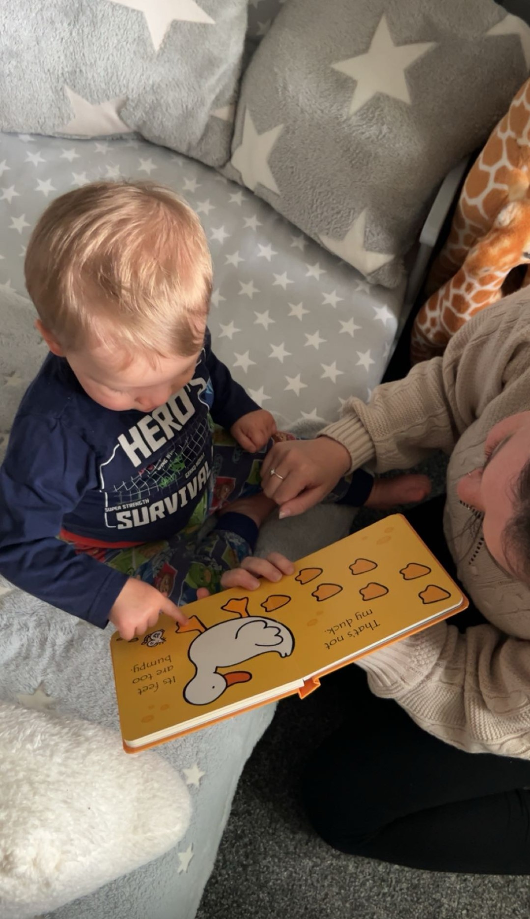 A child holding open a picture book with page showing a white duck and footprints in yellow background.